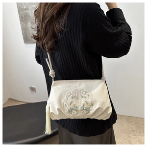 Detail of cream satin crossbody bag with floral embroidery and tassel on model