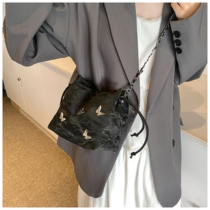 Detalle de bolso saco negro con cordón, mariposas plateadas 3D y correa de cadena