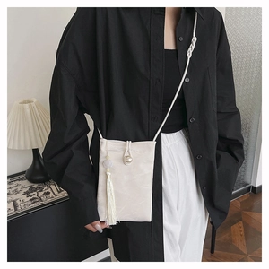 Detail of cream crossbody mini bag with pearl decor, white tassel and woven strap