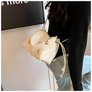 Detalle del bolso de cuero blanco crema con mariposas de metal plateado y cordón ajustable