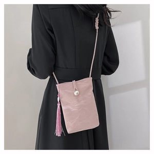 Pink crossbody bag with pleated texture, pearl button and tassel on black dress