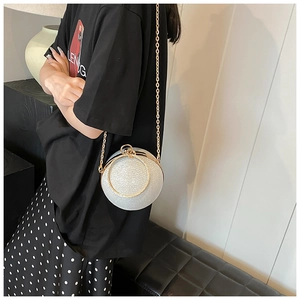 Detailed view of a silver glitter spherical bag with golden metal handle and chain strap
