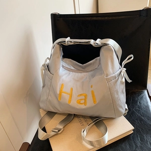 Detail of light blue nylon tote bag with yellow Hai embroidery and drawstring side ties
