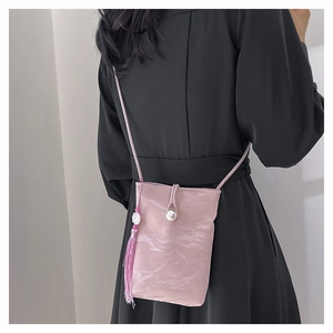 Pink crossbody bag with pearl clasp and floral tassel on a black dress backdrop