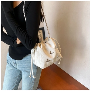 Detalle de bolso bucket plisado blanco roto con dije de mariposa y correa de cadena