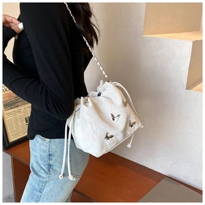 Detalle del bolso de hombro blanco con dijes de mariposa y correa de cadena plateada