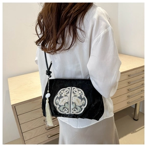 Detail of a black embroidered crossbody bag with white silk tassels and jade bead accents