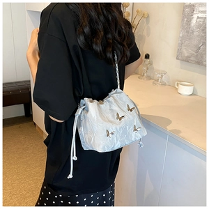 Detalle de bolso saco azul claro con mariposas metálicas, cordón y cadena transparente
