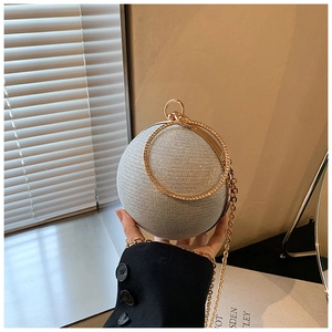 Close-up of sparkling silver spherical clutch bag with golden ring handle and chain