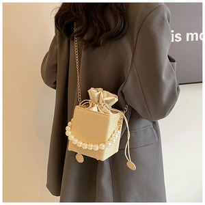 Detail of straw woven bucket bag with large pearl handle and golden chain strap