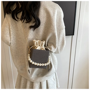 Détail d'un sac seau en tissu gris avec poignée en perles et chaîne dorée sur un modèle