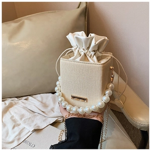 Detail of beige woven crossbody bag with pearl handle and golden chain strap