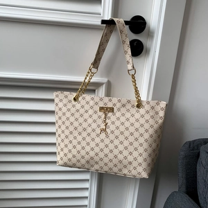 Beige floral printed tote bag with gold chain strap and deer charm on white door
