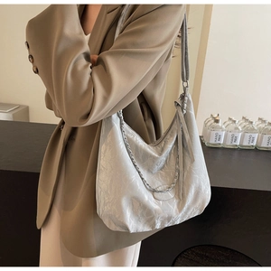 Silver wrinkled leather tote bag with chain strap shown on model in cafe setting