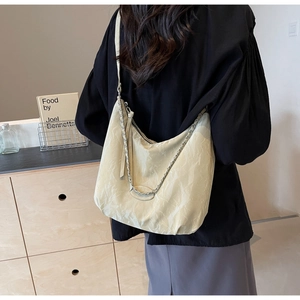 Detail of off-white pleated PU leather crossbody bag with chain strap worn by a model