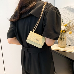 Minimalist beige straw crossbody bag with golden chain and lock shown on a model
