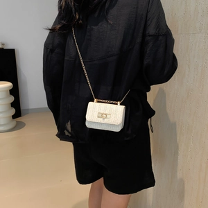 Minimalist beige woven crossbody bag with gold chain strap shown on model's shoulder