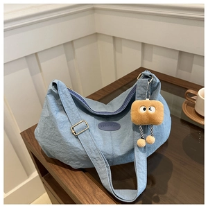 Detail of blue canvas tote bag with a small brown plush doll charm on a wooden table