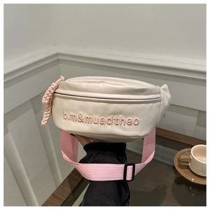 Détail du sac banane crème avec broderie rose et décoration de breloque tressée