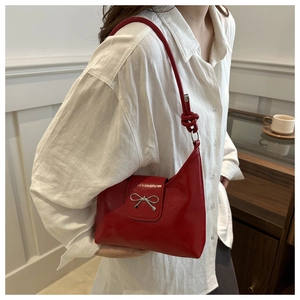 Detail of red glossy shoulder bag with silver metallic bow and knotted strap detail