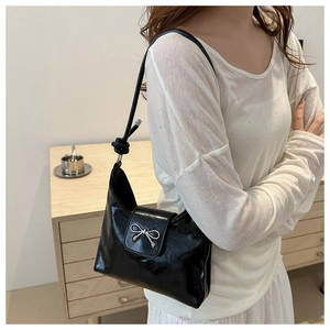 Close-up of black glossy leather underarm bag with silver bow buckle and knot strap detail