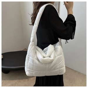 Side view of a white quilted puffer tote bag with wide shoulder strap on a model