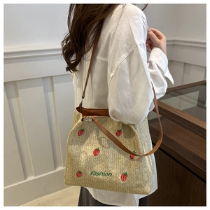 Détail de broderie fraise sur sac cabas en paille porté à l'épaule par un mannequin