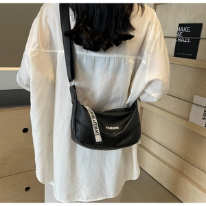 Detail of black faux leather crossbody bag featuring fashion woven labels and wide strap