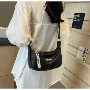 Detail of black pebbled crescent bag with FASHION label and HOMME+FEMME webbing strap