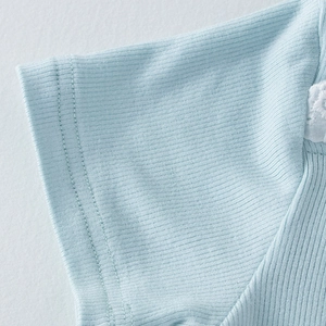 Détail du tissu côtelé bleu clair avec broderie en dentelle blanche sur l'épaule