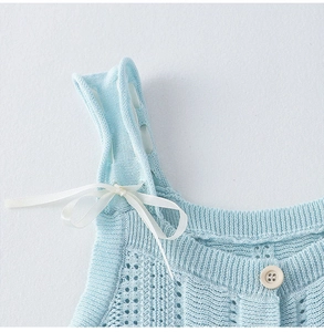 Dettaglio gilet in maglia azzurro con ricamo, fiocco di nastro e bottone in legno