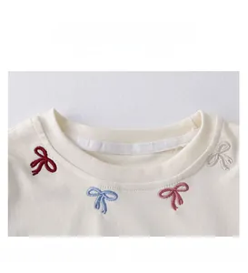 Detail of girls' cotton top featuring four-color bow embroidery and ribbed neckline