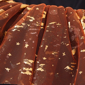 Detailed macro view of orange mesh fabric with golden stars for girls' ballet dress