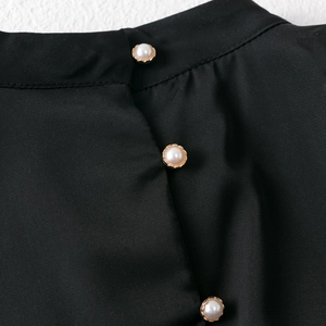 Detail of black dress neckline with three elegant faux pearl buttons and gold trim