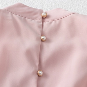 Detail of three pearl buttons with golden edges on the back of a pink dress for girls