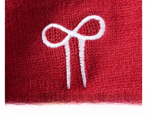 Détail de la broderie de nœud blanc sur un pull en tricot rouge pour filles