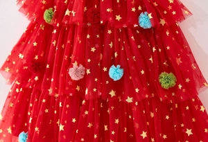 Detail of red tutu dress with gold stars and colorful pom poms on soft mesh fabric