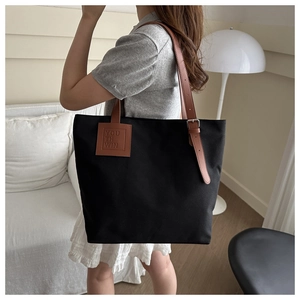 Detail view of large black canvas tote bag with brown leather straps worn on shoulder