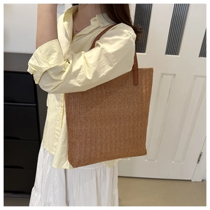 Detail view of woven straw tote bag with brown leather handles and wavy texture