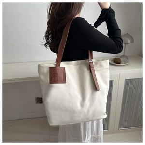 Close-up of minimalist canvas tote bag featuring brown leather trim and YO TH WIN patch