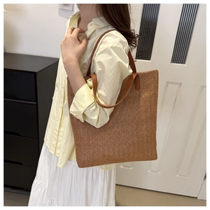 Detailed side view of a large woven straw tote bag with brown leather handles worn by a model