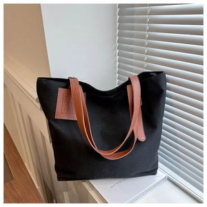 Close-up of black canvas tote bag with brown straps and leather patch on window sill