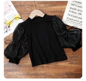 Detail of girl's black sweater featuring elegant sheer puff sleeves and delicate bow ties