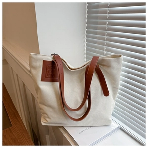 Detail of canvas tote bag with brown leather straps and side logo patch on a window sill