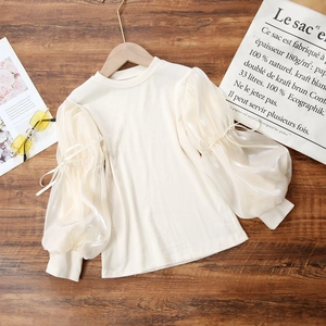 Detail of girls' cream knit top featuring sheer puff sleeves and delicate bow accents