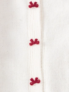 Détail du tricot blanc avec de petits nœuds en velours rouge sur le pull pour enfant