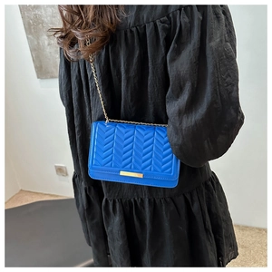 Detail of bright blue V-quilted crossbody bag with gold chain strap on black dress