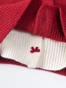 Détail du nœud tricoté rouge et texture côtelée blanche sur le pull pour fille