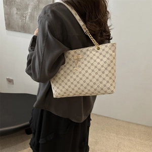 Chic beige tote bag with geometric diamond patterns and gold chain strap on a model