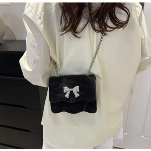 Détail du mini sac noir à bords ondulés avec nœud argenté et chaîne porté par un modèle
